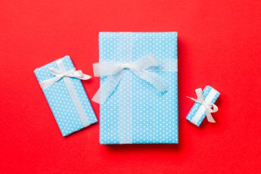 Kırmızı arka planda beyaz kurdeleli Noel veya diğer tatil hediyelerini kağıda sardım. Hediye kutusu, hediye dekorasyonu renkli masa, üst görünüm