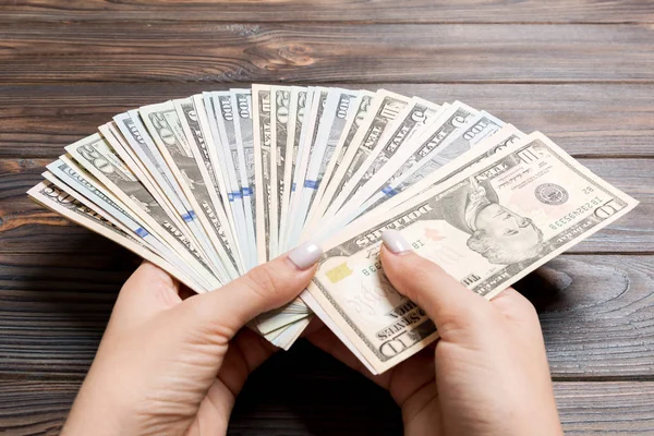 Perspektivní pohled na ženskou ruku držící na dřevěném podkladu vějíř s penězi. 100 dolarové bankovky. Koncepce úvěrů a dluhů — Stock fotografie