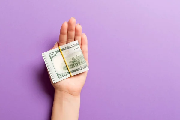 Vista superior de la mano femenina sosteniendo una gran cantidad de billetes en dólares enrollados sobre un fondo colorido. Concepto de pobreza. Concepto de crédito con espacio de copia — Foto de Stock