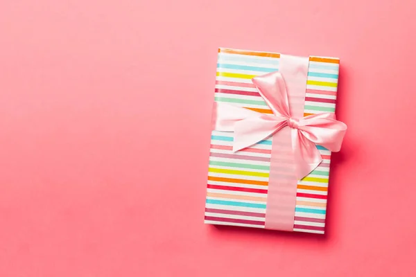 用粉红缎带包裹在活珊瑚背景上的圣诞礼物或其他手工制作的节日礼物。 礼物盒，彩色桌子上的礼物装饰，顶部有复印空间 — 图库照片