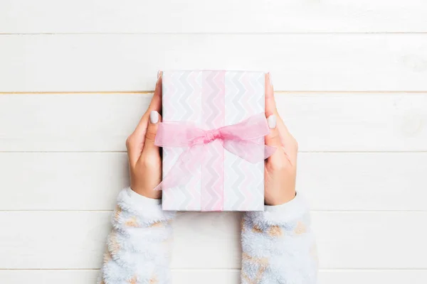 Woman arms holding gift box with colored ribbon on white wooden table background, top view and copy space for you design