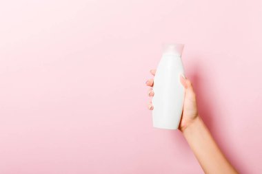 Kadın el tutarak krem şişe losyon izole. Kız pembe arka plan üzerinde tüp kozmetik ürünleri vermek