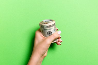 Kadın eli sıkıca bir tomar para tutuyor. Renkli arka planda en iyi 20 dolarlık manzara. Yatırım kavramı