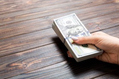 Kadın el ahşap arka plan üzerinde yüz dolarlık banknotlar bir demet tutan. Fotokopi alanı ile maaş ve ücret kavramı