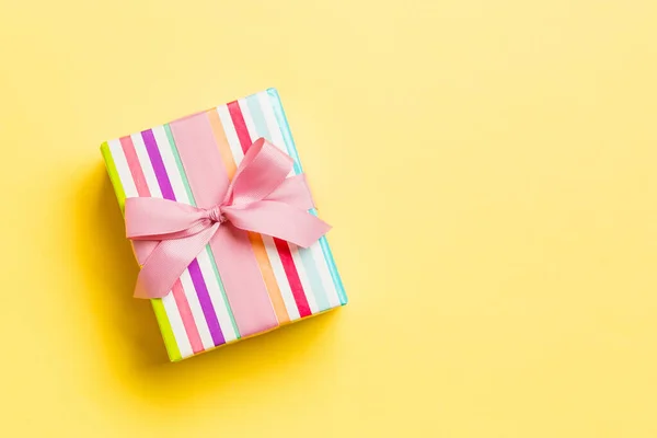 Envuelto Navidad u otro regalo hecho a mano de vacaciones en papel con cinta rosa sobre fondo amarillo. Caja de regalo, decoración de regalo en mesa de colores, vista superior con espacio para copiar — Foto de Stock