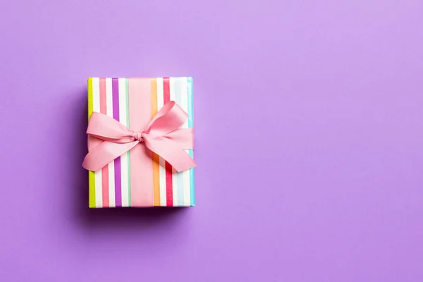 用紫色背景粉红缎带的纸包裹圣诞节或其他节日手工制作的礼物。 礼物盒，彩色桌子上的礼物装饰，顶部有复印空间 — 图库照片