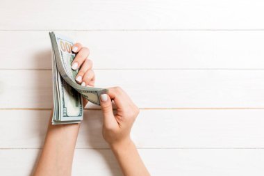 İş kadınının elleri tahtadan arka planda 100 dolarlık banknotları sayıyor. Fotokopi alanı ile maaş ve ücret kavramı. Yatırım konseptinin en üst görünümü