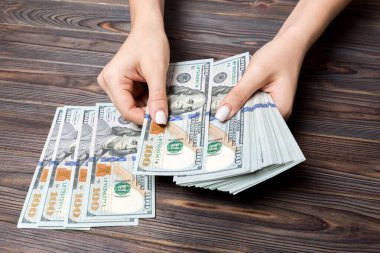 Para sayan kadın ellerinin perspektif görünümü. Ahşap arka planda 100 dolarlık banknotlar. İş kavramı