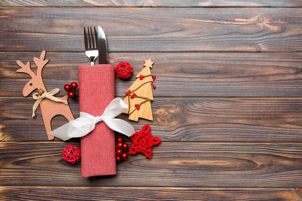 Top view of holiday objects on wooden background. Utensils tied up with ribbon on napkin. Christmas decorations and reindeer with copy space. New year dinner concept
