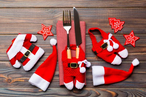 Feestelijke set vork en mes op houten ondergrond. Bovenaanzicht van nieuwjaar decoraties en santa kleding en hoed. Close up van het kerstconcept — Stockfoto