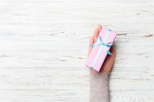 Kvinna armar hålla presentförpackning med färgat band på vit rustik trä bord bakgrund, ovanifrån och kopiera utrymme för dig design — Stockfoto