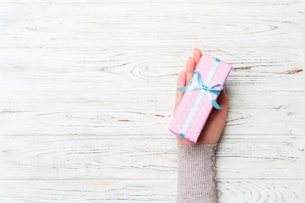 Brazos de mujer sosteniendo caja de regalo con cinta de color sobre fondo de mesa de madera rústica blanca, vista superior y espacio de copia para su diseño — Foto de Stock