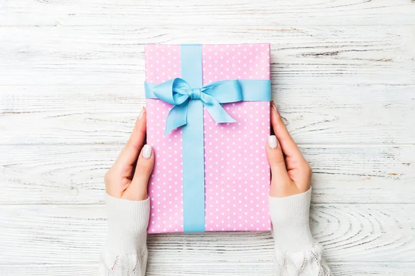 Vista dall'alto donna mani in possesso di scatola regalo con fiocco colorato su sfondo in legno rustico bianco con spazio copia — Foto Stock