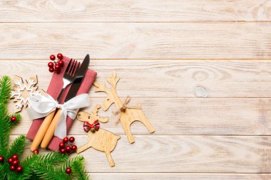 Tahta arka plandaki tatil eşyalarının üst görüntüsü. Utensiller peçeteye kurdele ile bağlanmış. Noel süsleri ve fotokopi alanı olan ren geyikleri. Yeni yıl yemeği konsepti