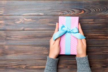 Koyu ahşap masa arkasında renkli kurdeleli hediye paketi olan kadın kolları, üst görünüm kopya alanı