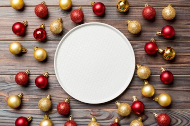 Ahşap zemin üzerinde kırmızı ve altın takılar bulunan şenlikli tabağın en üst görüntüsü. Noel süslemeleri ve oyuncakları. Yeni Yıl Geliştirme kavramı