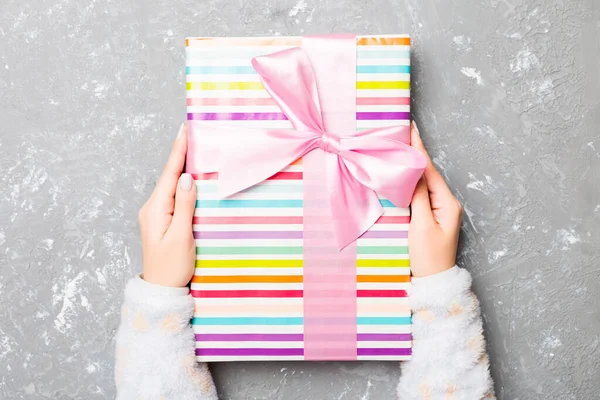 Woman arms holding gift box with colored ribbon on gray cement table background, top view and copy space for you design — Stock Photo, Image