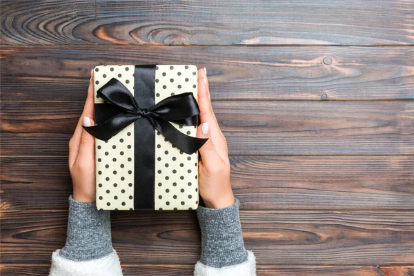 Γυναικεία χέρια που κρατούν ριγέ κουτί δώρου με χρωματιστή κορδέλα σε σκούρο ρουστίκ ξύλινο φόντο. Χριστουγεννιάτικο concept ή άλλο χειροποίητο κουτί δώρου διακοπών, concept top view με χώρο αντιγραφής — Φωτογραφία Αρχείου