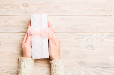 Kadın elleri renkli kağıda sarılı Noel veya diğer tatil hediyelerini verir. Hediye kutusu, hediye süsü sarı kırsal ahşap masa, fotokopi alanı olan üst manzara.