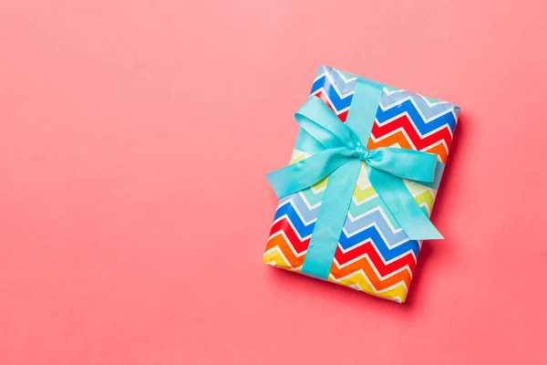 Avvolto Natale o altra vacanza fatto a mano presente in carta con nastro blu su sfondo corallo vivente. Scatola regalo, decorazione del regalo sulla tavola colorata, vista dall'alto con spazio di copia — Foto Stock