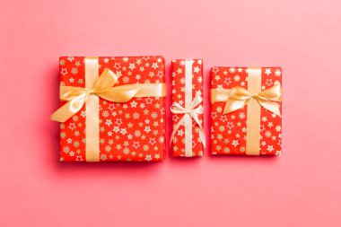 Yaşayan mercan arka planında altın kurdeleyle kağıda sarılmış Noel veya diğer tatil hediyeleri. Hediye kutusu, hediye dekorasyonu renkli masa, üst görünüm