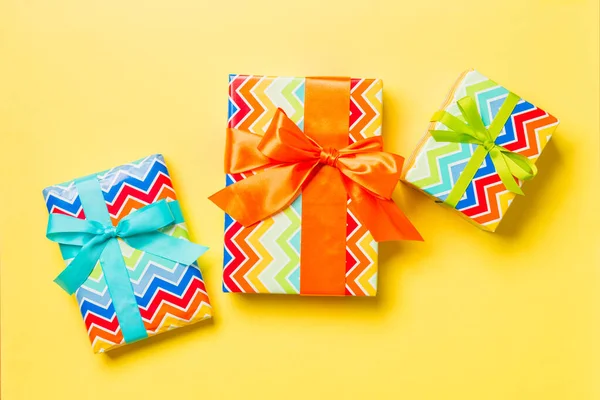 Geschenkdoos met blauwe, groene en oranje strik voor Kerstmis of Nieuwjaar op gele achtergrond, bovenaanzicht — Stockfoto