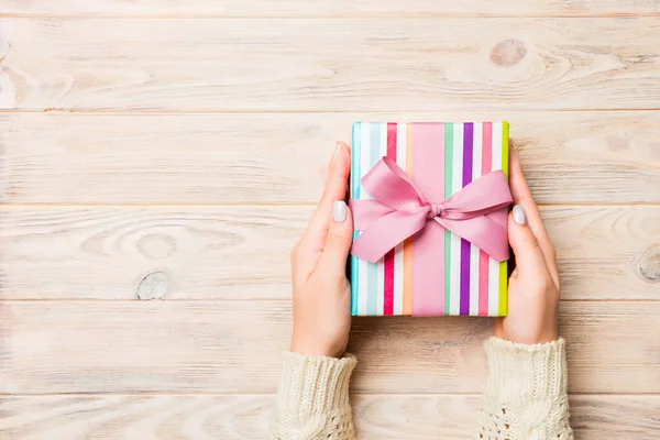 Fille mains tenant boîte cadeau en papier artisanal avec comme cadeau pour Noël ou d'autres vacances sur fond jaune rustique en bois, vue du dessus avec sppace copie — Photo