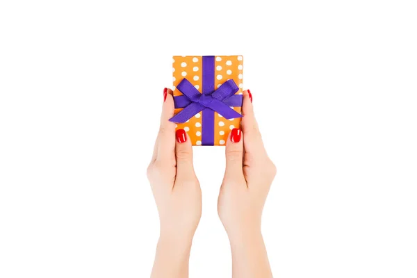 Vrouw handen geven verpakt Kerstmis of andere vakantie met de hand gemaakt in oranje papier met paars lint. Geïsoleerd op witte achtergrond, bovenaanzicht. dankzegging Geschenkdoos concept — Stockfoto
