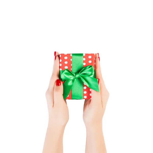 女性の手は緑のリボンで赤い紙に包まれたクリスマスや他の休日の手作りプレゼントを与える。白い背景に、上部のビューに隔離された。感謝祭のギフトボックスコンセプト — ストック写真