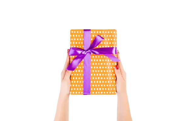Kvinnliga händer ger insvept jul eller annan semester handgjorda present i orange papper med lila band. Isolerad på vit bakgrund, ovanifrån. Thanksgiving Gift box koncept — Stockfoto