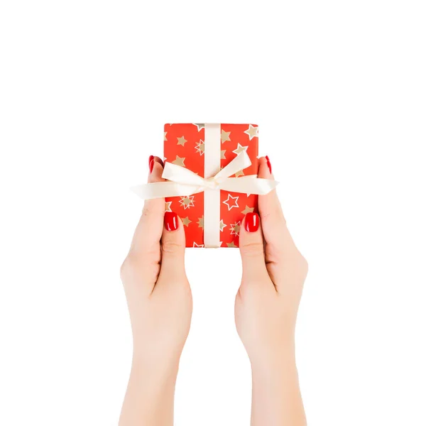 Dámské ruce dát zabalené vánoční nebo jiné sváteční ručně vyrobené dárek v červeném papíru se zlatou stuhou. Izolované na bílém pozadí, horní pohled. koncept díkůvzdání dárkové krabice — Stock fotografie
