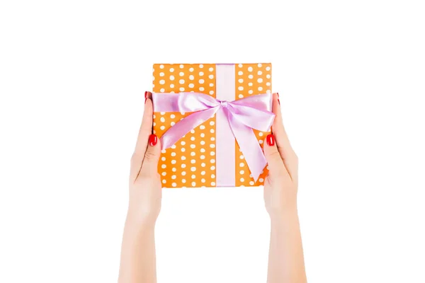Vrouw handen geven verpakt Kerstmis of andere vakantie met de hand gemaakt in oranje papier met paars lint. Geïsoleerd op witte achtergrond, bovenaanzicht. dankzegging Geschenkdoos concept — Stockfoto