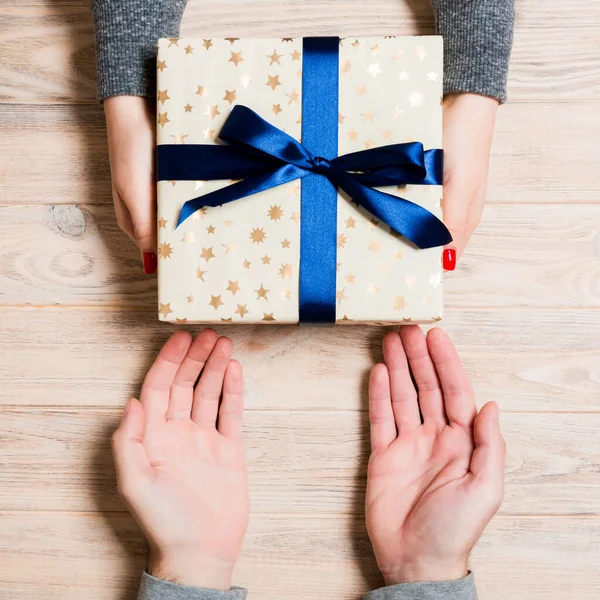 Bovenaanzicht van het geven en ontvangen van een cadeau op houten ondergrond. Een man en een vrouw die een geschenk in handen hebben. Close-up van feestelijk concept — Stockfoto