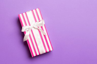 Noel veya Yeni Yıl için beyaz fiyonklu hediye kutusu mor arka planda, fotokopi alanı olan üst görünüm