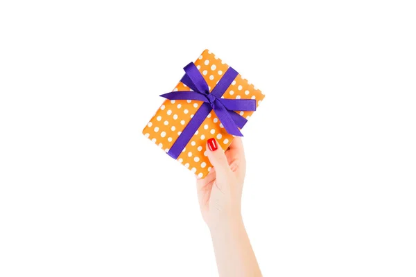 Woman hands give wrapped Christmas or other holiday handmade present in orange paper with purple ribbon. Isolated on white background, top view. thanksgiving Gift box concept — Stock Photo, Image
