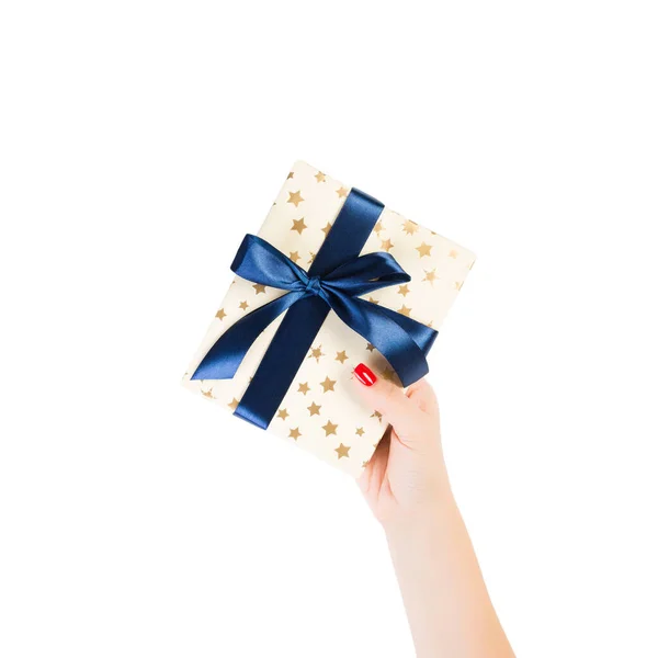 Vrouw handen geven verpakt Kerstmis of andere vakantie met de hand gemaakt in goud papier met blauw lint. Geïsoleerd op witte achtergrond, bovenaanzicht. dankzegging Geschenkdoos concept — Stockfoto