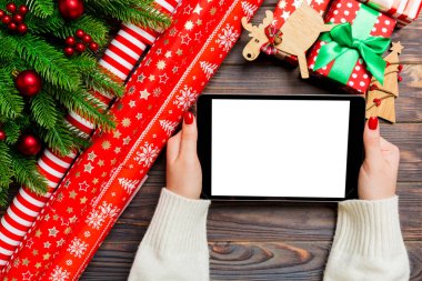 Kadın ellerinin, köknar ağacı ve şenlikli süslemelerden yapılmış ahşap Noel arka planında bir tablet taşıdığı en üst görüntü. Yeni yıl tatili konsepti. Model