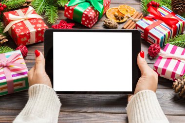 Kadın ellerinin, köknar ağacı ve şenlikli süslemelerden yapılmış ahşap Noel arka planında bir tablet taşıdığı en üst görüntü. Yeni yıl tatili konsepti. Model