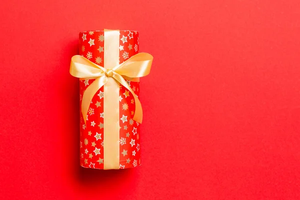 Τυλιγμένο Χριστούγεννα ή άλλες γιορτές χειροποίητο δώρο σε χαρτί με χρυσή κορδέλα σε κόκκινο φόντο. Παρουσιάστε το κιβώτιο, διακόσμηση του δώρου στο χρωματιστό τραπέζι, top view με το διάστημα αντιγράφων — Φωτογραφία Αρχείου
