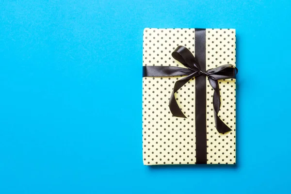 Verpakt Kerstmis of andere met de hand gemaakte vakantie cadeau in papier met zwart lint op blauwe achtergrond. Aanwezig doos, decoratie van geschenk op gekleurde tafel, bovenaanzicht met kopieerruimte — Stockfoto