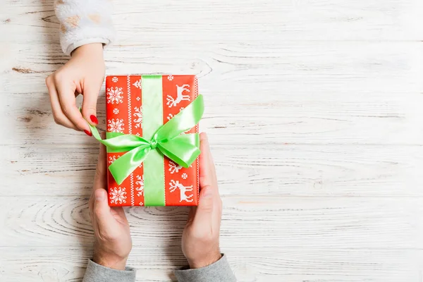 Bovenaanzicht van het geven en ontvangen van een geschenk op houten achtergrond. Aanwezig in mannelijke en vrouwelijke handen. Liefdesconcept. Kopieerruimte — Stockfoto