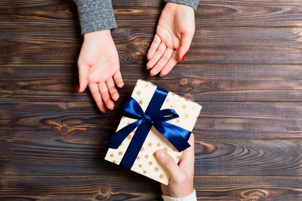 Bovenaanzicht van een vrouw en een man die een cadeau geven en ontvangen op een houten achtergrond. Liefde en relatie concept. Sluiten. — Stockfoto