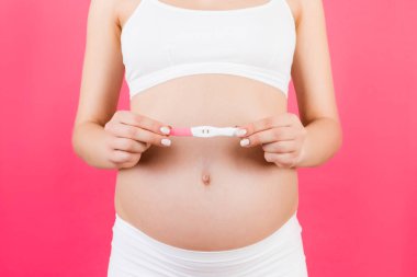 Pembe arka planda hamile kadının karnına yapılan pozitif hamilelik testini kapat. Beyaz iç çamaşırlı müstakbel anne. Bebek bekliyor. Boşluğu kopyala.