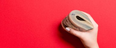 Kadın eli sıkıca bir tomar para tutuyor. Renkli arka planda 50 doların ve çeşitli dolarların üst görüntüsü. Kopya alanı ile yatırım kavramı.