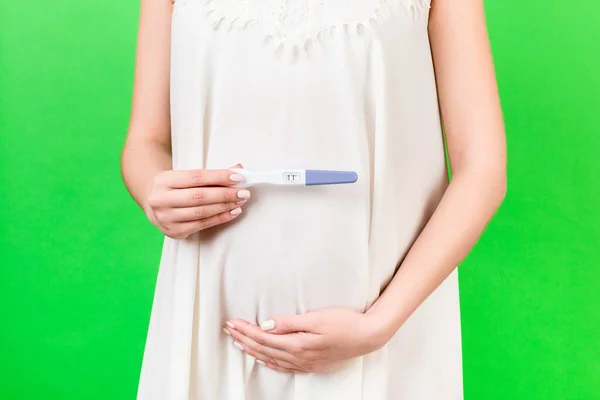 緑色の背景で陽性の妊娠検査を保持白いドレスの妊婦のクローズアップ 母親の概念 スペースのコピー — ストック写真