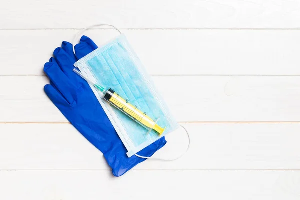 Top view of disposable surgical mask, pair of latex medical gloves and syringe on wooden background. Protect your health concept with copy space.
