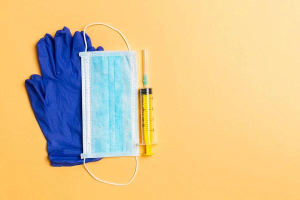 Top view of disposable surgical mask, pair of latex medical gloves and syringe on orange background. Protect your health concept with copy space.