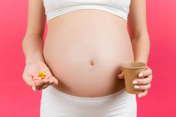 让孕妇一手拿着一杯水 一手拿着一堆药丸 背景五彩斑斓 有复制的空间 怀孕期间吃药的概念 — 图库照片