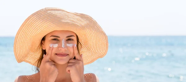 Pretty woman protects her skin on face with sunblock at the beach.