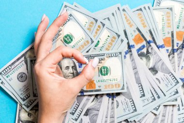 Bir elinde yüz dolarlık banknotların üst görünümü ve renkli arka plan üzerinde başka bir el ile tamam jest gösteren. Refah ve servet kavramı.